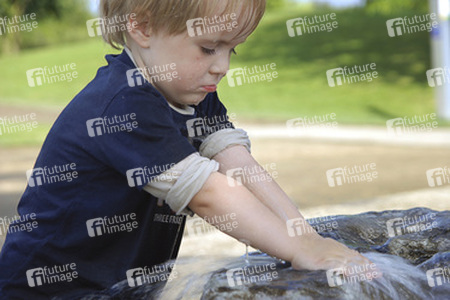 Junge spielt mit Wasser an einem Brunnen