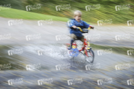 Kleinkind fährt mit Fahrrad durch eine Pfütze