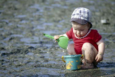 Kleinkind spielt am Meer im Watt mit Schaufel und Eimer