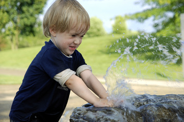 Junge spielt mit Wasser an einem Brunnen
