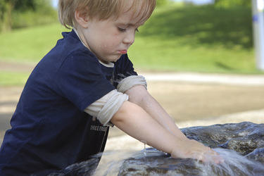 Junge spielt mit Wasser an einem Brunnen