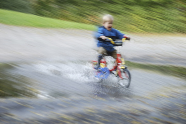 Kleinkind fährt mit Fahrrad durch eine Pfütze